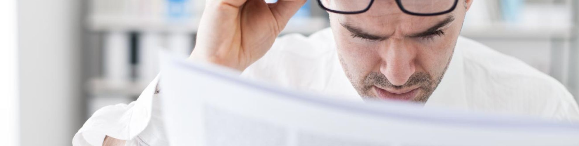 Homme lisant un journal en tenant ses lunettes de vu sur son front